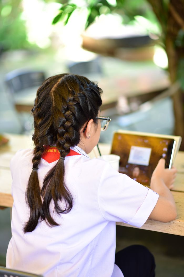 Back view of a young girl with braids using a tablet outside, focused on learning.