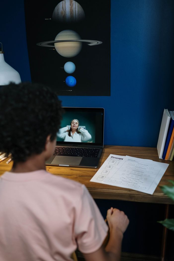 A child engaging in online learning at home with lesson papers and a laptop.