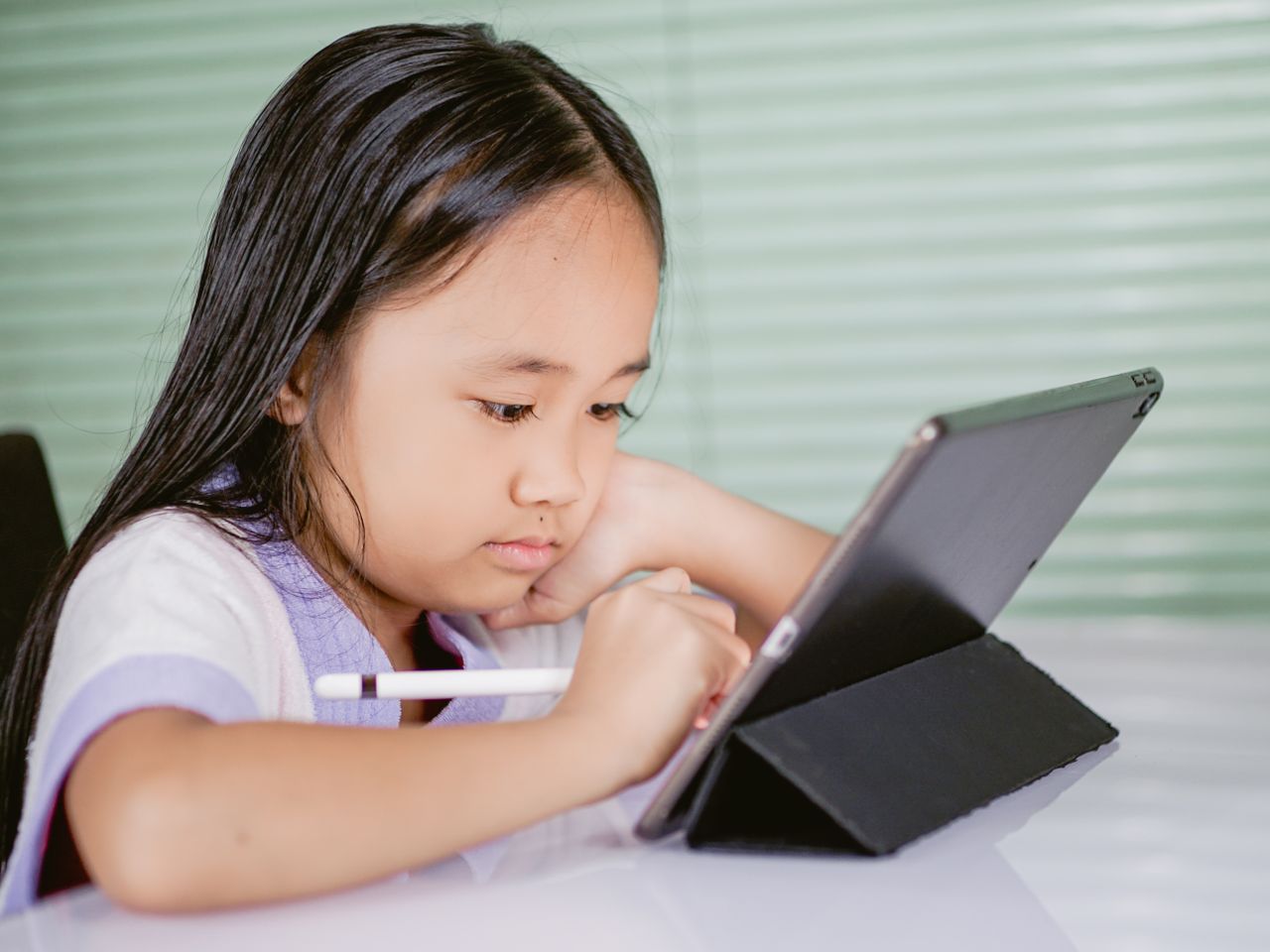 services-06 A young girl using a tablet for online learning, focused and engaged with her digital pen.