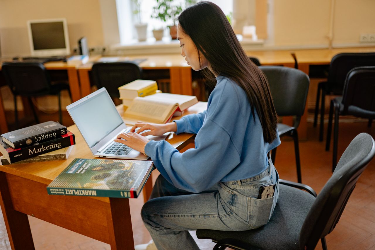 why-choose-us Focused woman typing on laptop, surrounded by books in a cozy study spot.
